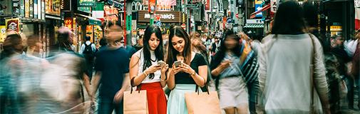 2 girls on streets of Japan looking at mobile devices