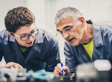 An elderly man teaching a young man