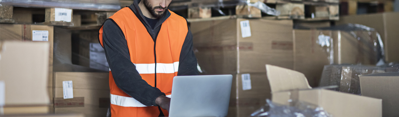 man in shipping warehouse on laptop