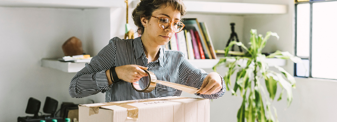 woman taping up a package in her home office