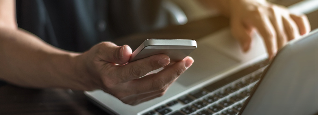 person looking at a mobile phone while using a laptop