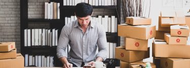 man in home office with stacks of boxes for shipping around him