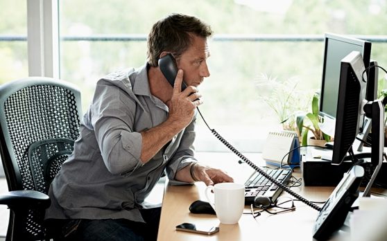 man in home office looking at computer screen while on the phone