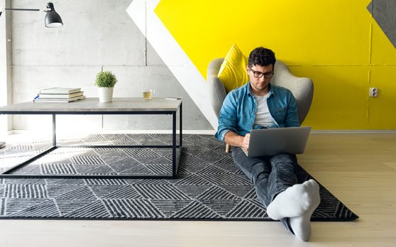 man sitting on the floor of a home office working on a laptop 