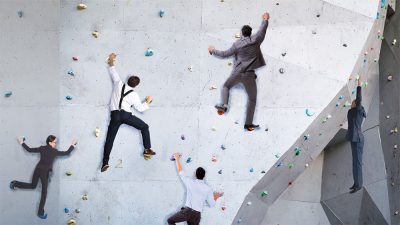 men in business suits ascending a climbing wall